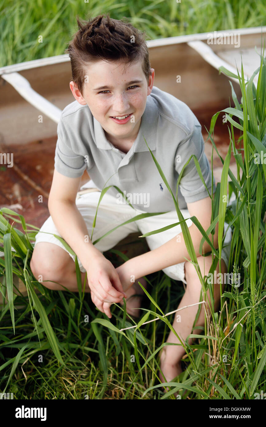 Boy (12-13) crouching on grass near boat Stock Photo