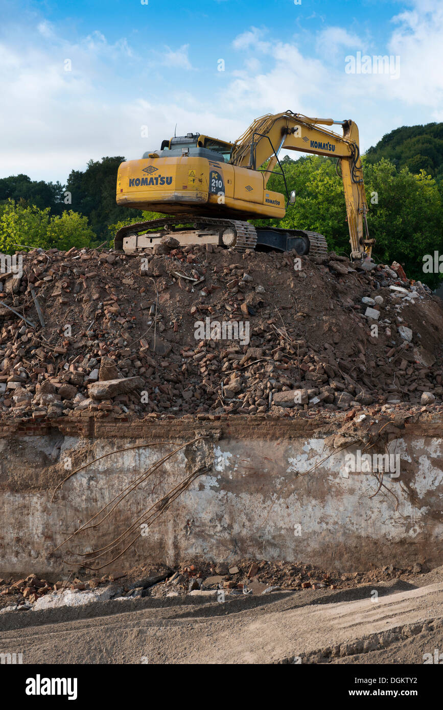Excavator standing on a large rubble heap, clearing the demolition site ...