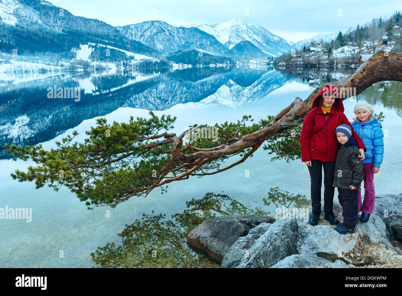 Cloudy winter Alpine lake Grundlsee view (Austria) with fantastic pattern-reflection on water and family under pine twig. Stock Photo