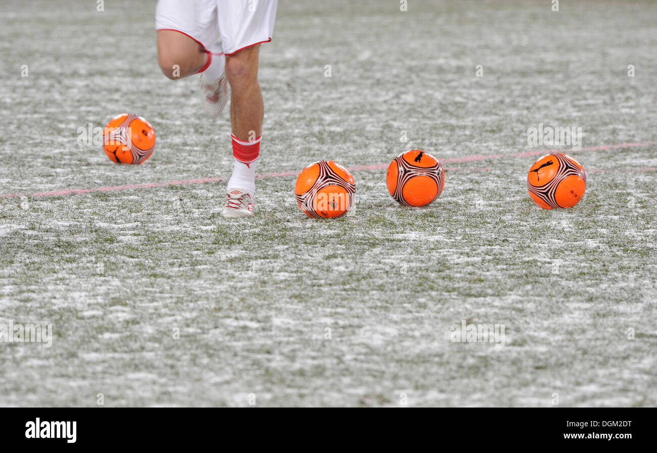 Warm-up training with orange footballs for the winter on snow-covered pitch Stock Photo