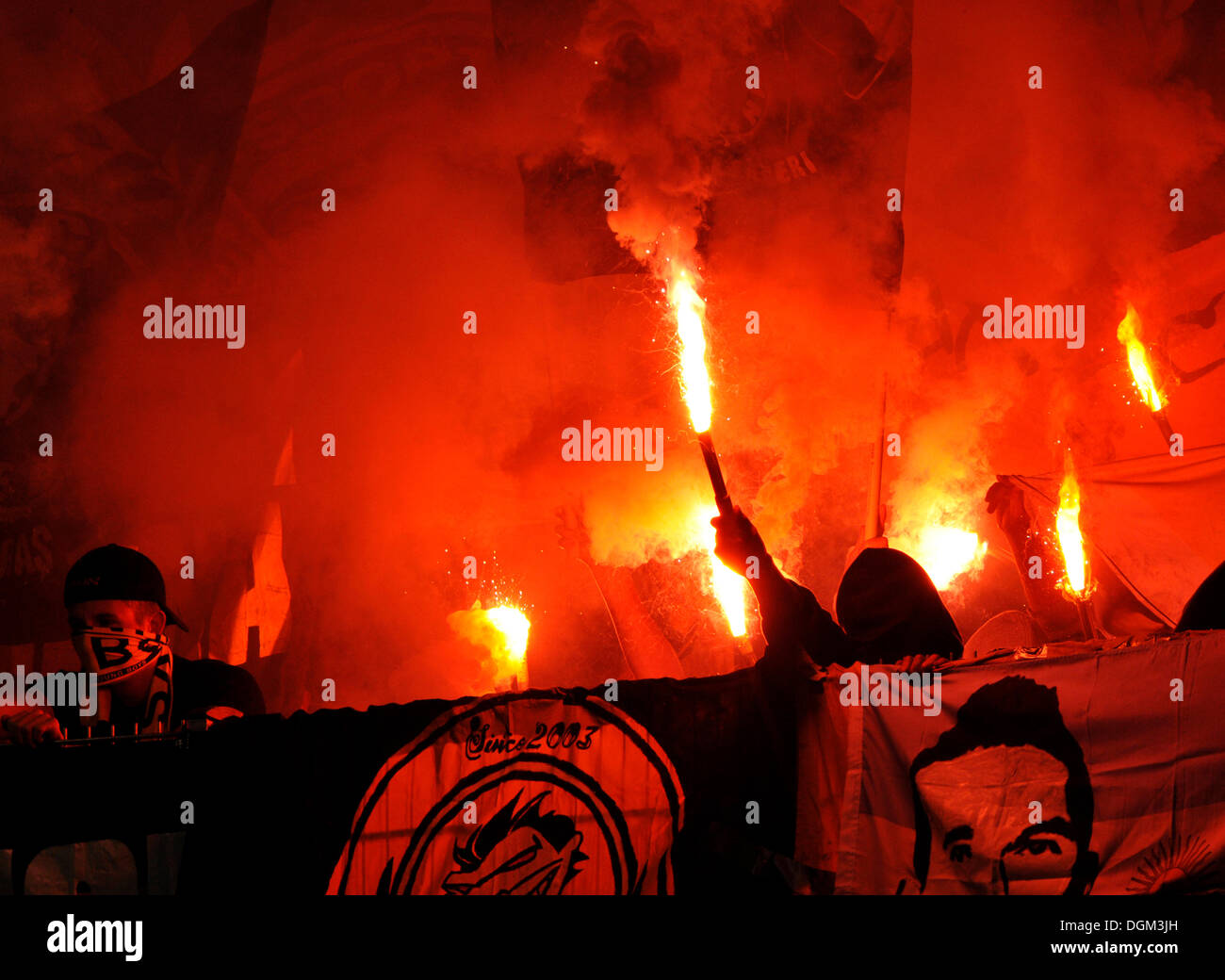 Violent, masked supporters igniting flares in a stadium fan block Stock Photo