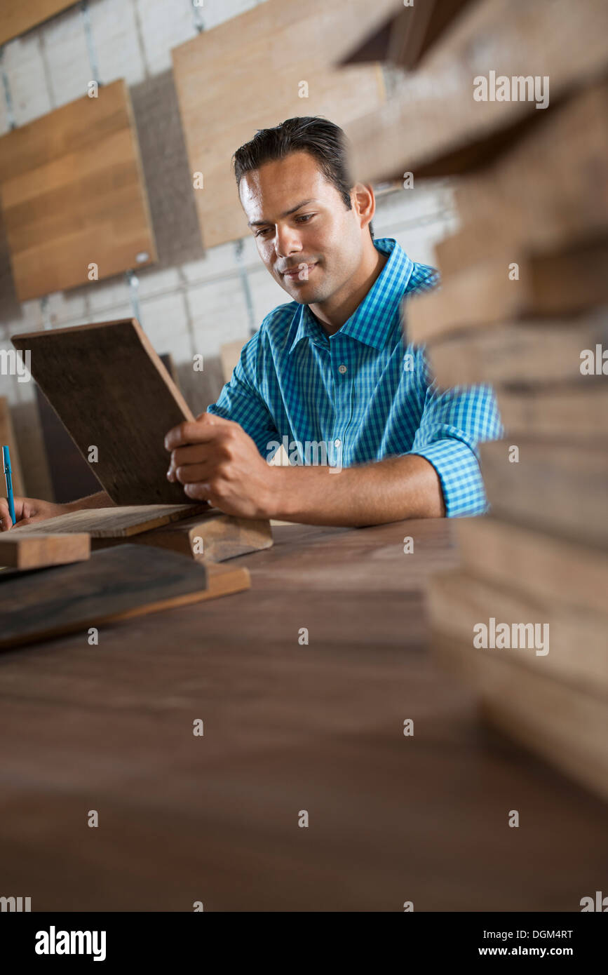 A young man in a workshop. Examing a wood sample and taking notes on paper. Stock Photo