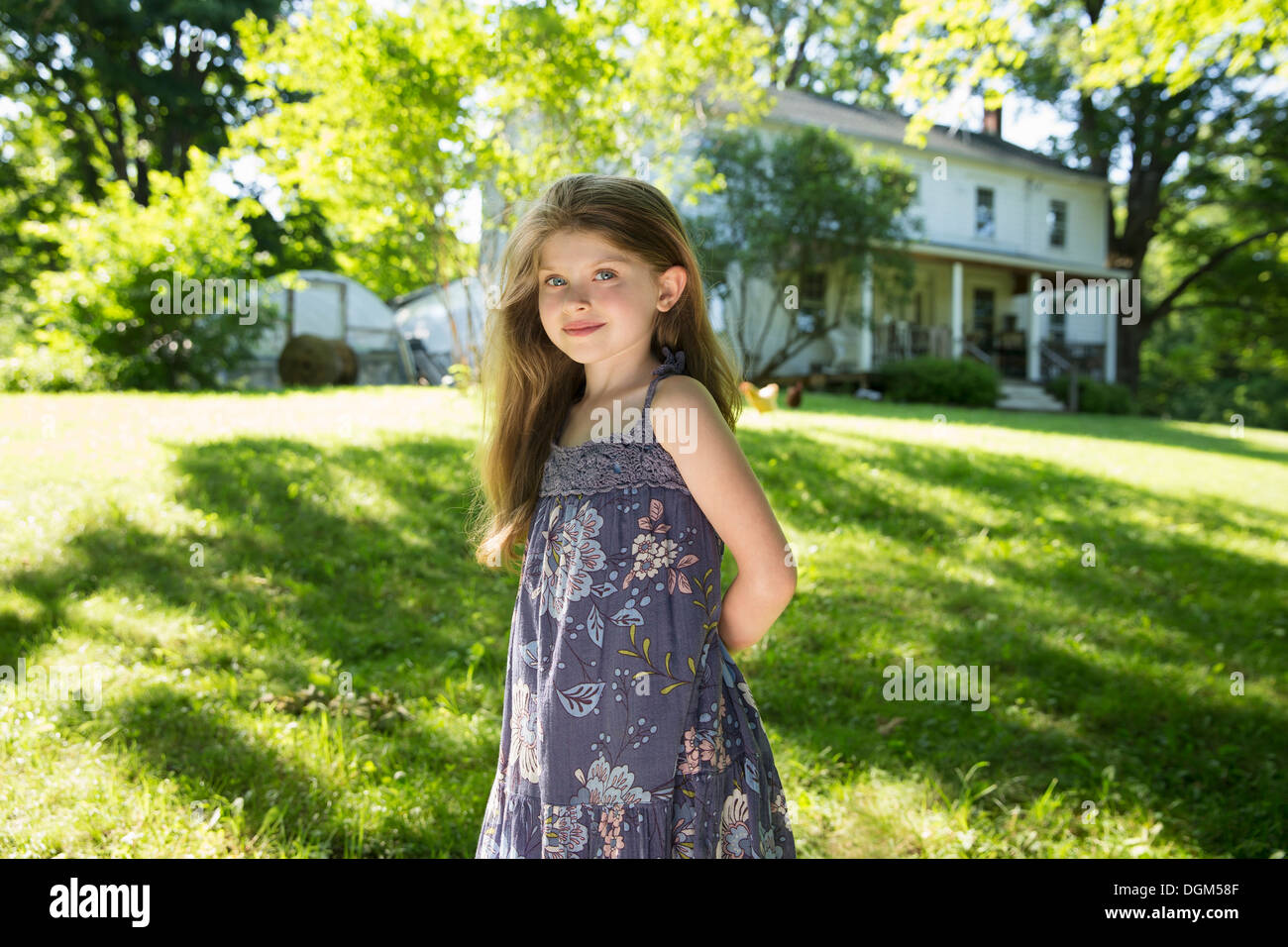 Outdoors in summer. On the farm. A girl in the garden with her hands behind her back. Stock Photo