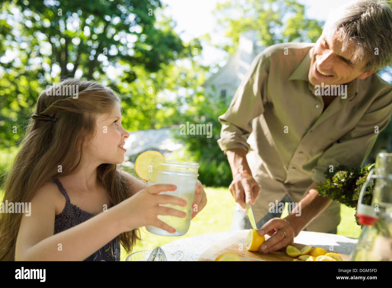 On the farm. Children and adults working together. A girl and an adult man making lemonade. Cutting up fresh fruits. Stock Photo