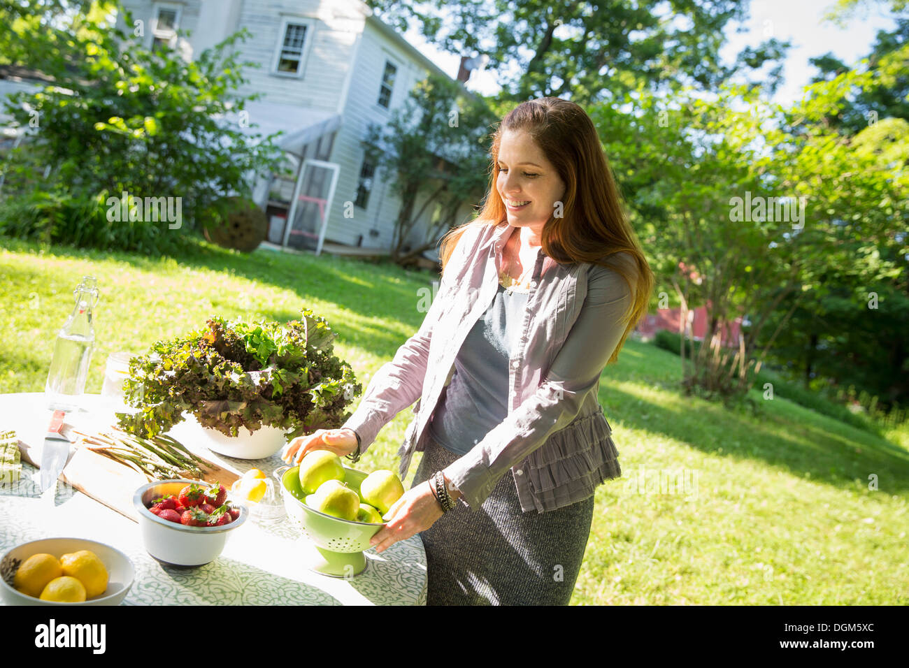 On farm woman in farmhouse garden preparing table fresh organic foods fresh vegetables salads bowls of fresh fruit for meal Stock Photo