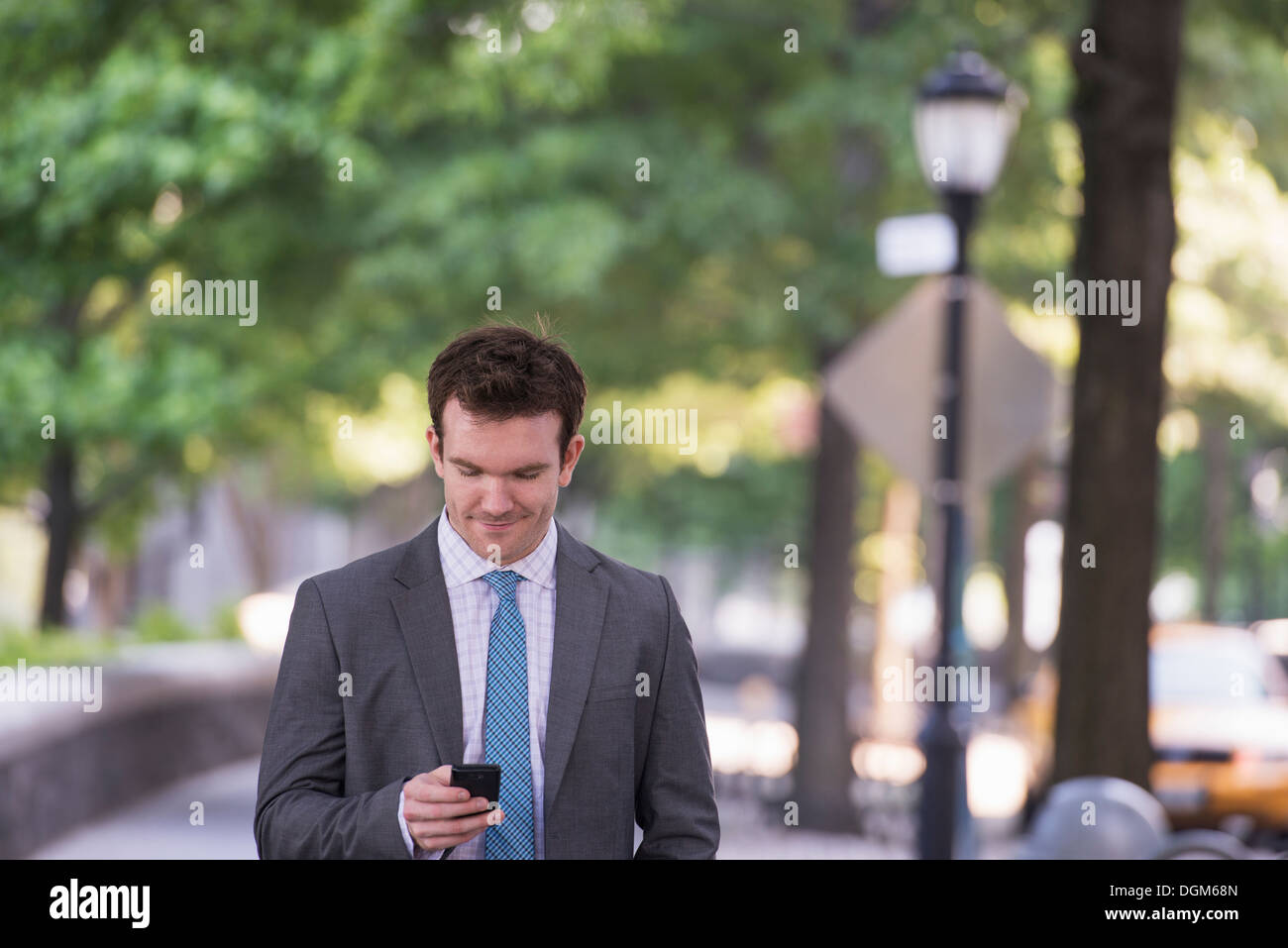 Summer. A young man in a grey suit and blue tie. Using a smart phone. Stock Photo