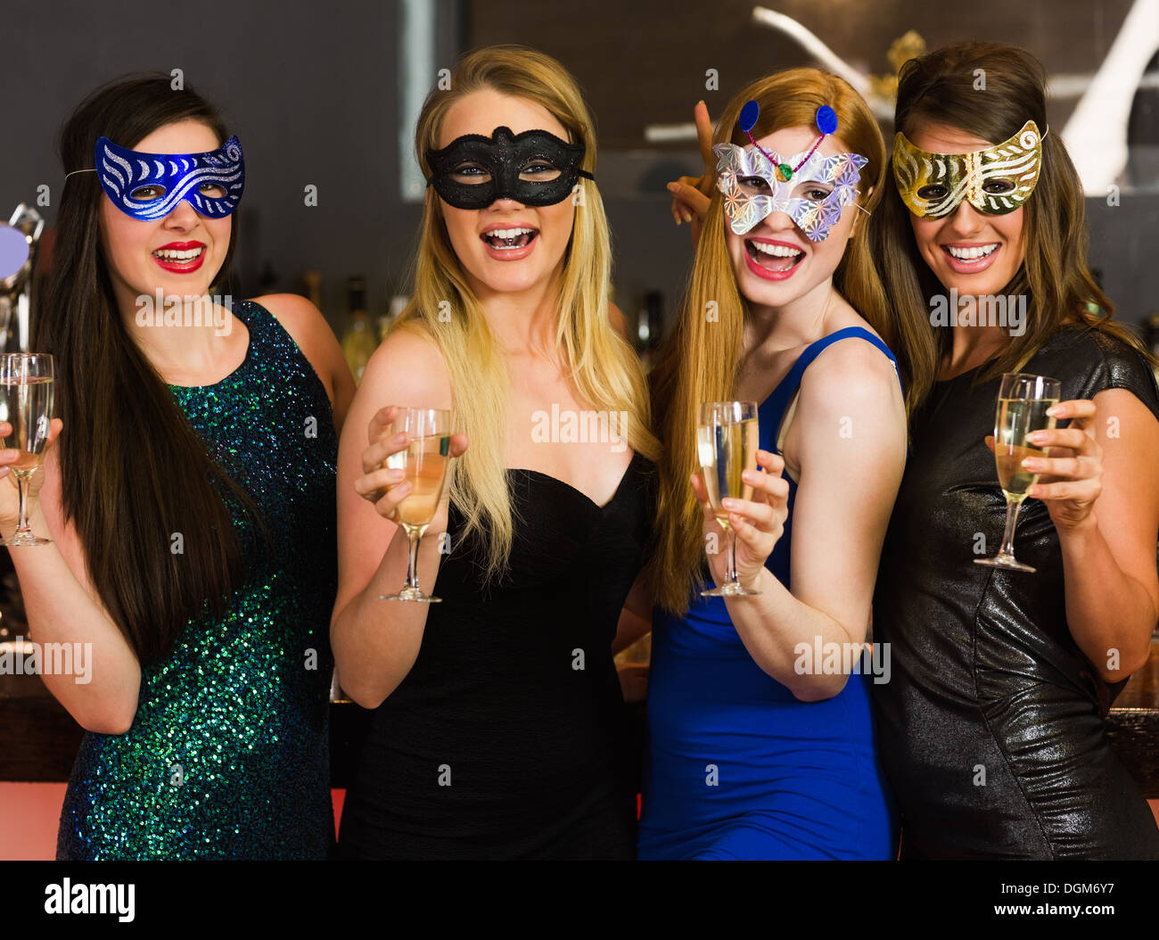 Laughing friends wearing masks holding champagne glasses Stock Photo