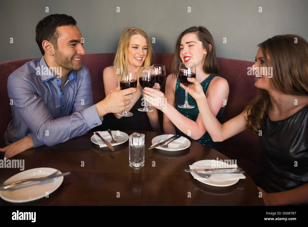 Laughing friends sitting together clinking glasses Stock Photo