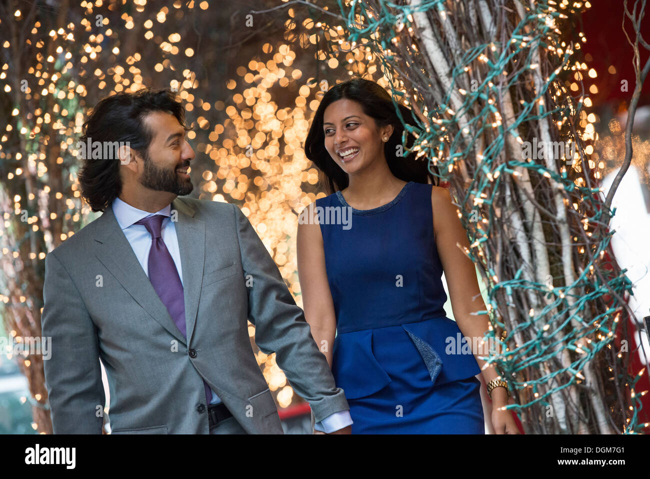Business people. Two people, a man and woman holding hands and walking under a pergola, lit with fairy lights. Stock Photo