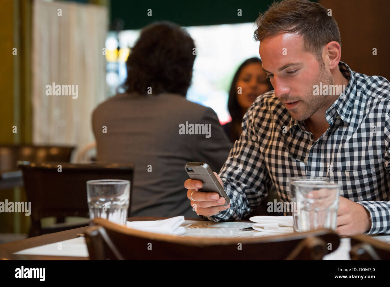 Business people. Two people talking to each other, and a man at a separate table checking his phone. Stock Photo