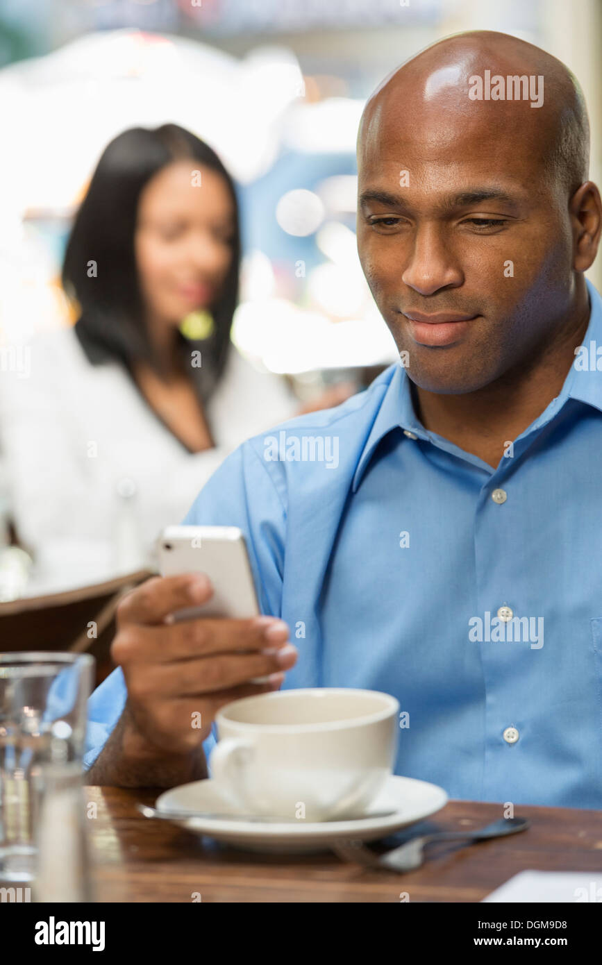 Business people. Two people sitting at coffee shop tables, checking their messages. Stock Photo