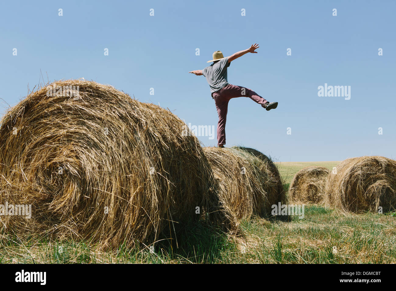Back view of a man balancing on one leg on top of a hay bale. Stock Photo