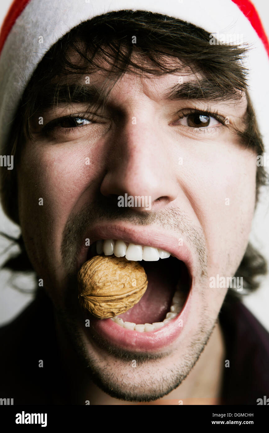 Young Man with a Santa hat, walnut between his teeth, nutcracker, Germany Stock Photo