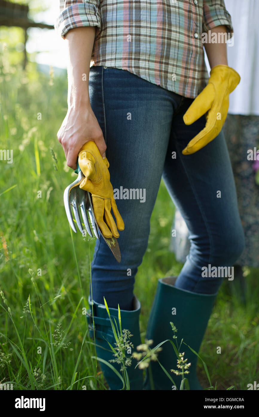 Organic farm. A worker wearing blue jeans, yellow thick gardening gloves holding a trowel. Stock Photo