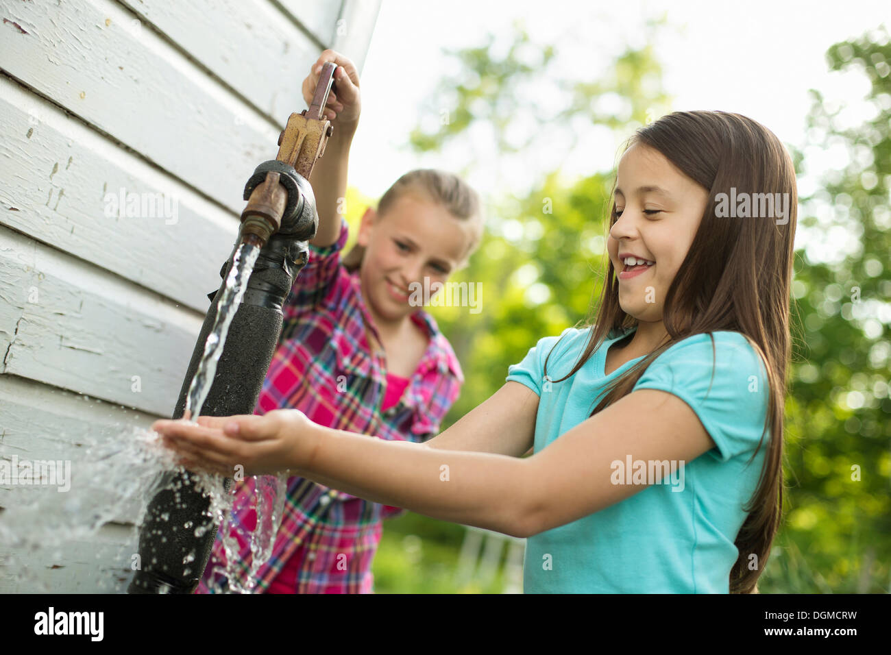 Organic farm. Two girls washing their hands under the flow of water from a pump in the yard. Stock Photo