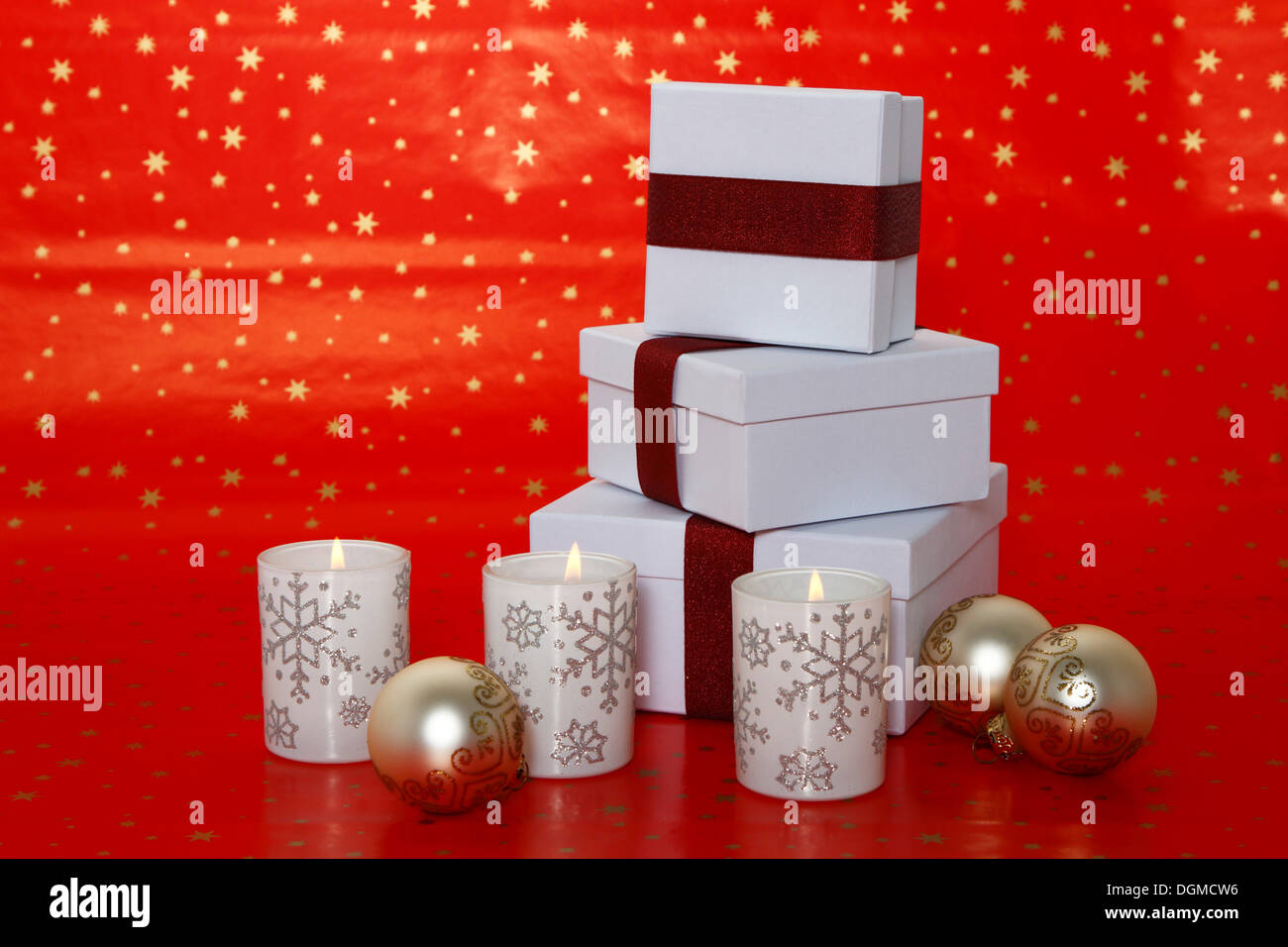 Burning candles standing on red Christmas wrapping paper, with presents and baubles Stock Photo