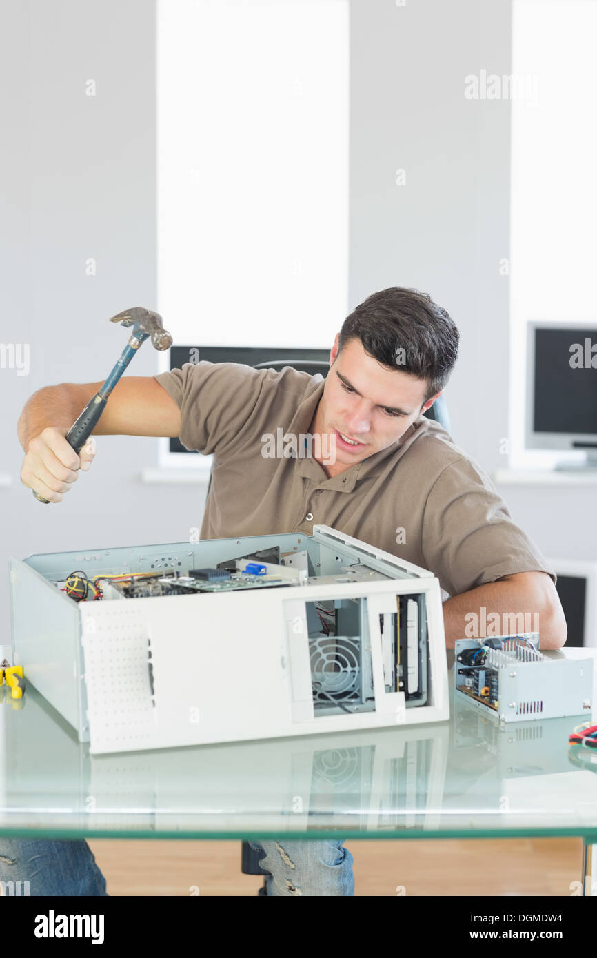 Handsome angry computer engineer destroying computer with hammer Stock Photo
