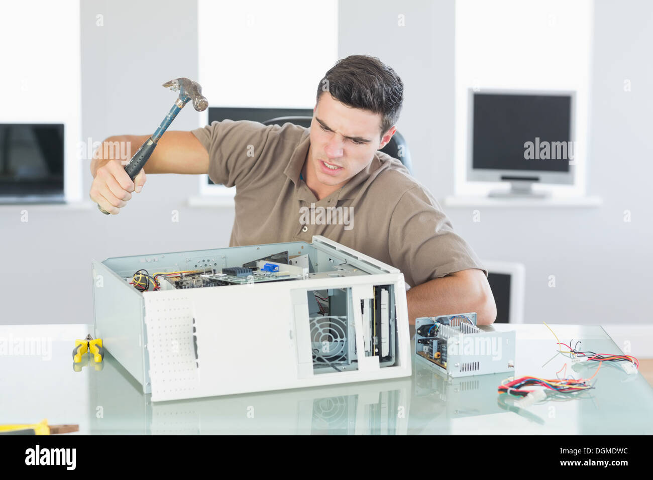 Attractive angry computer engineer destroying computer with hammer Stock Photo