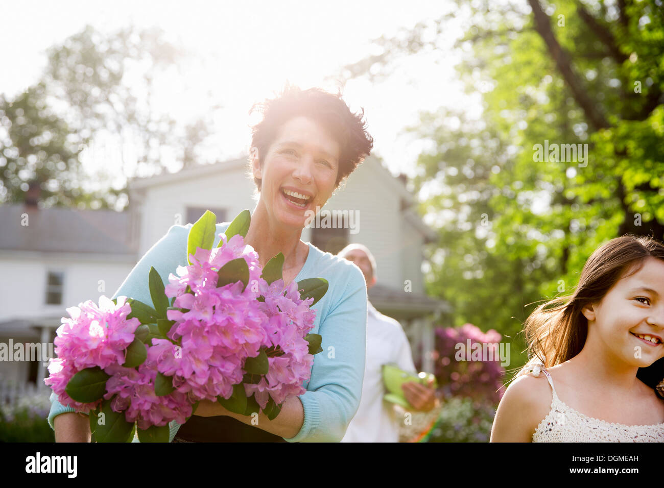 Family party. A woman carrying a large bunch of rhododendron flowers, smiling broadly. Stock Photo