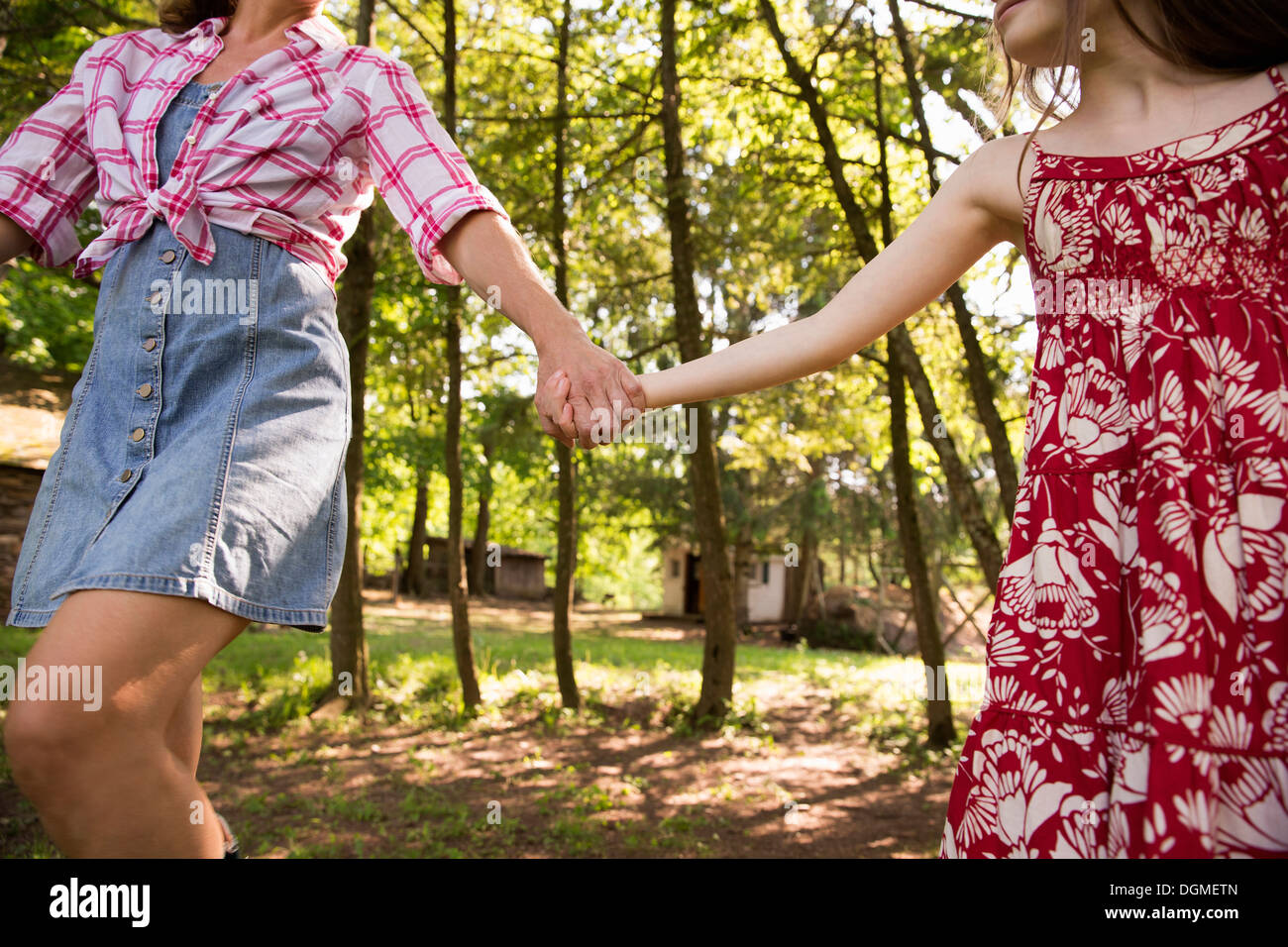 A woman and a young girl holding hands and running along under the trees. Stock Photo