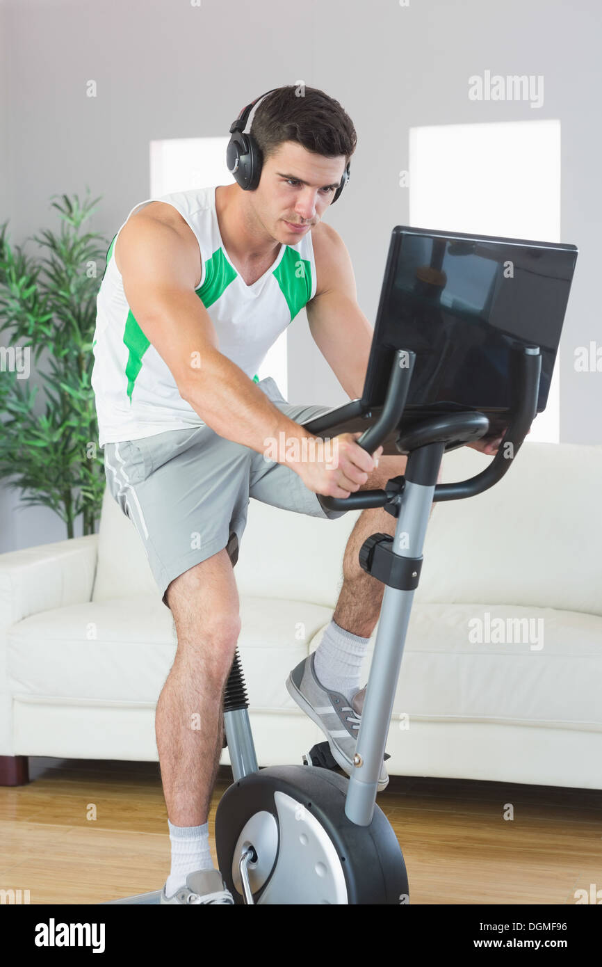 Determined handsome man training on exercise bike using laptop Stock Photo