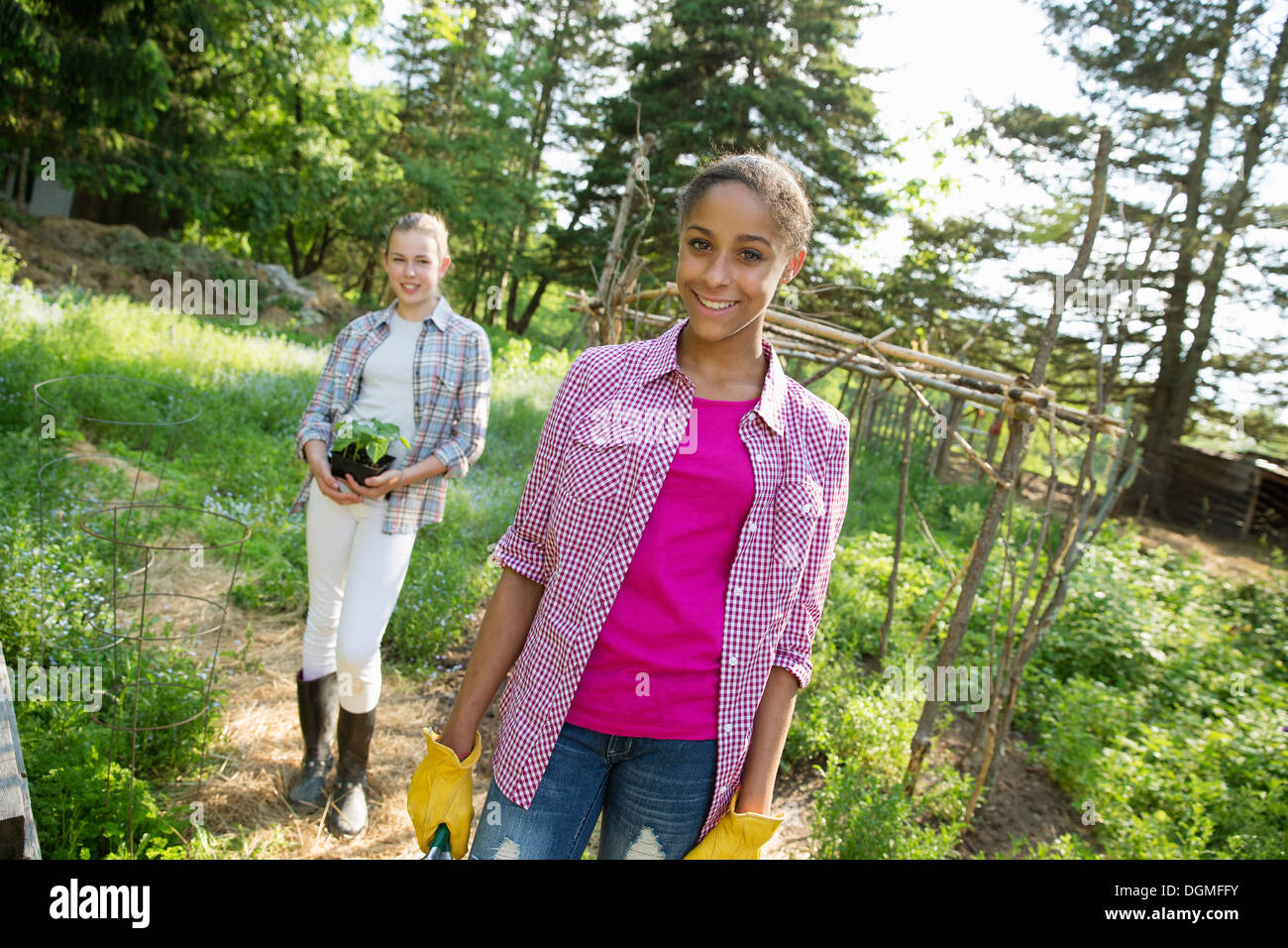 Two girls in a garden, walking up the path, one carrying a plant in a pot. Stock Photo