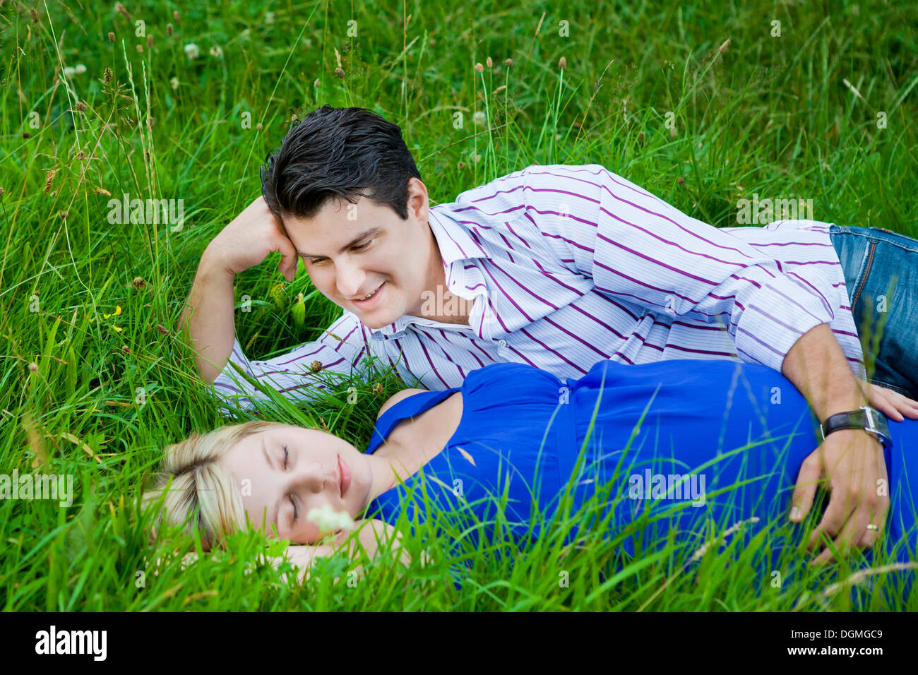 Man lying with his pregnant woman in the grass and looking at her tenderly Stock Photo