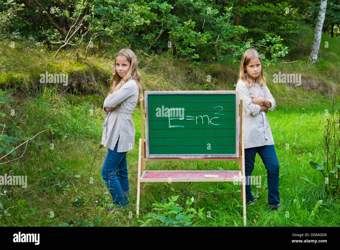 Twin girls, 9, looking annoyed beside a children's blackboard with Einstein's formula E = mc² Stock Photo
