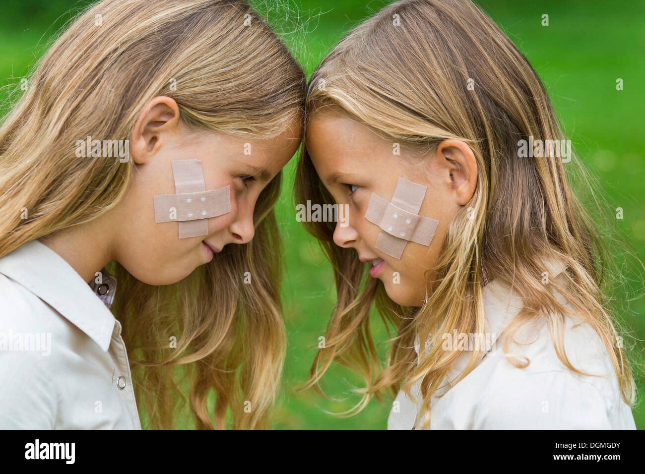Twin girls, 9, standing forehead to forehead, with plaster strips on their cheeks Stock Photo