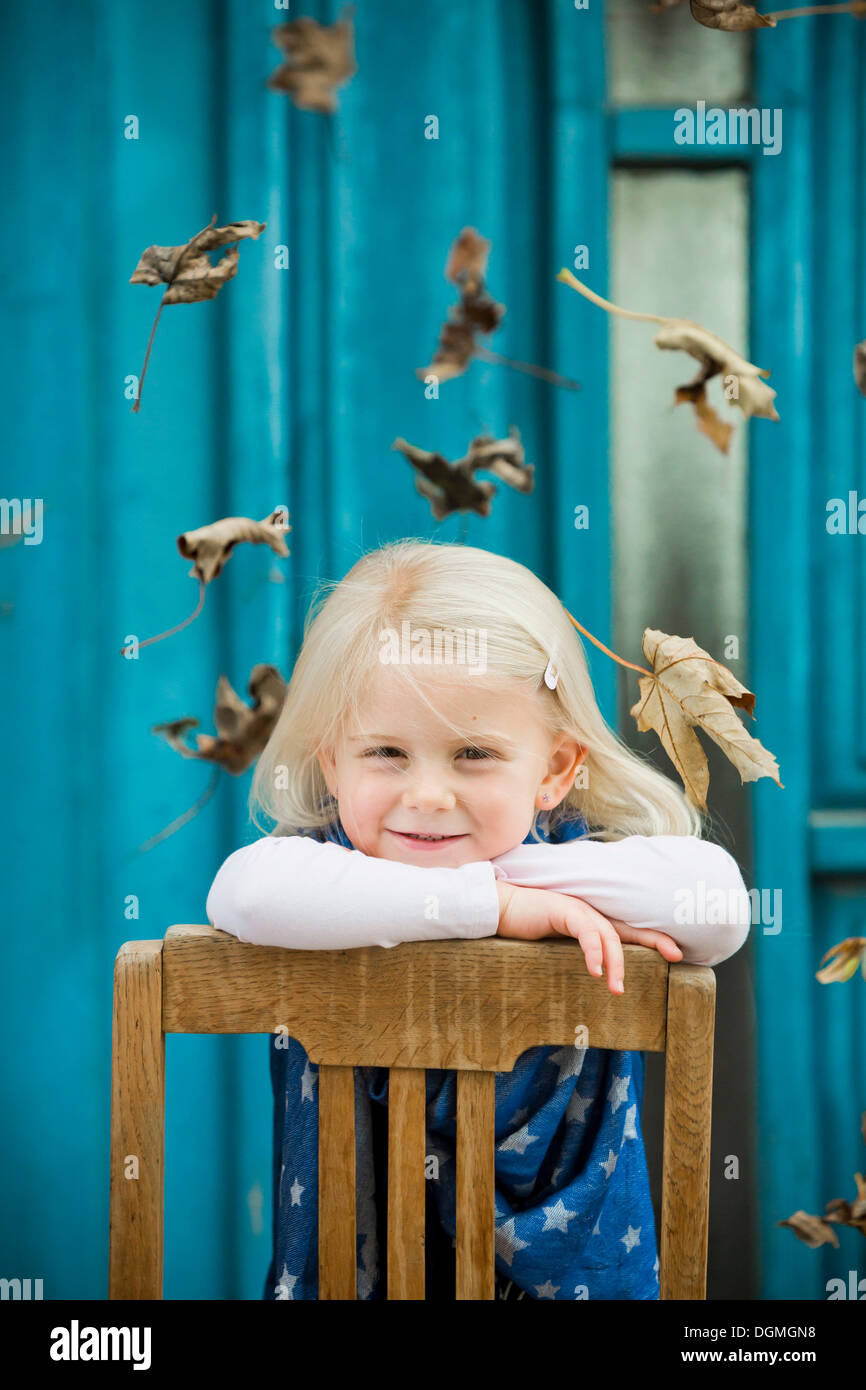 Girl, 4 years old leaning on a chair, leaves falling Stock Photo