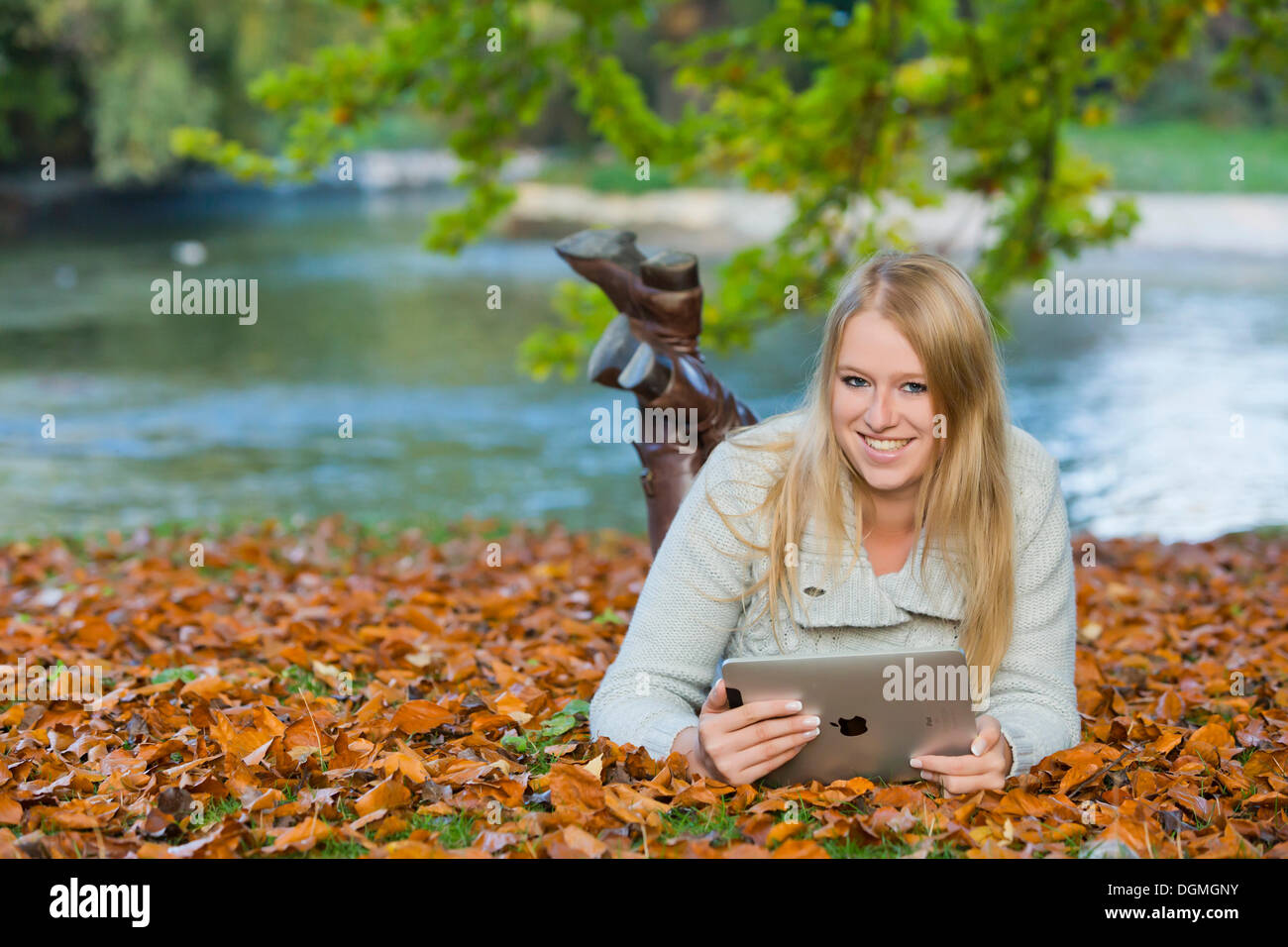 Young woman lying on her belly on the ground in a park and looking at a tablet PC Stock Photo