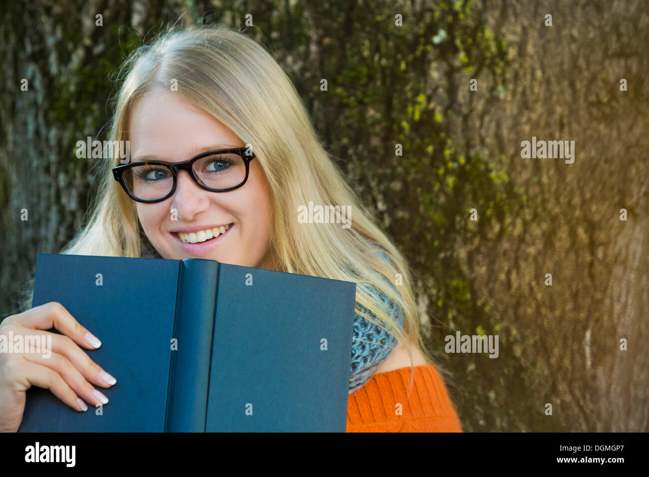 Young woman wearing glasses looking over the edge of a book Stock Photo