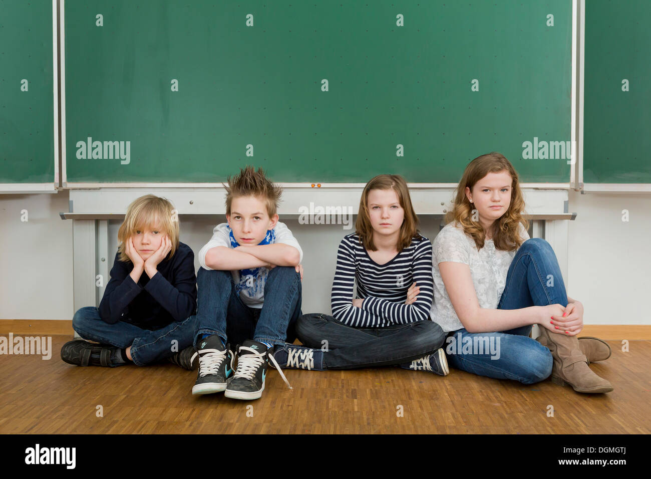 School children sitting bored in the classroom on the floor in front of the blackboard, Germany Stock Photo