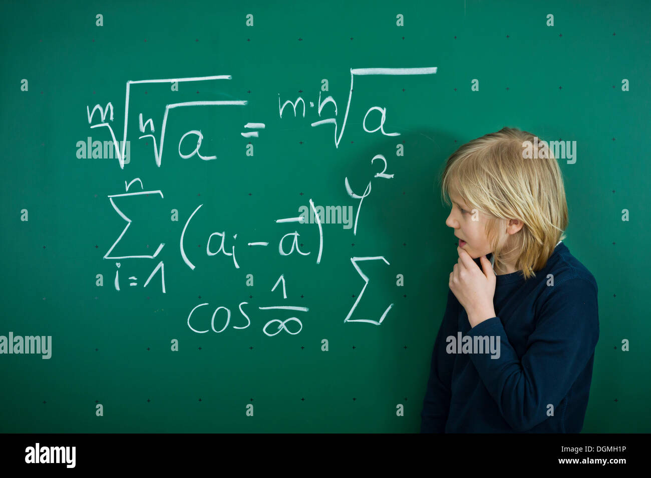 Schoolboy pondering a mathematical formula on a school blackboard, Germany Stock Photo