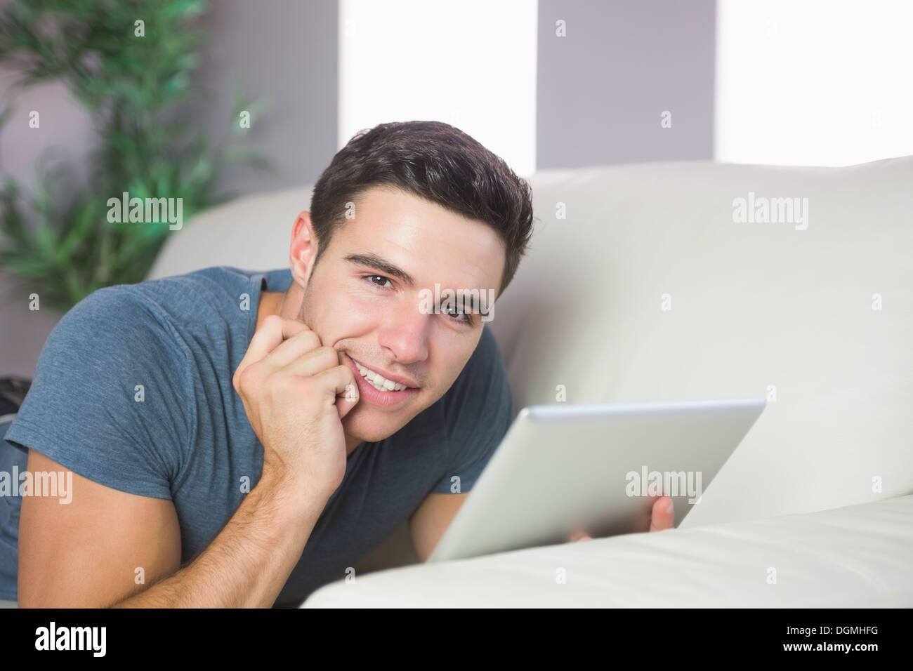 Smiling handsome man lying on couch using tablet Stock Photo