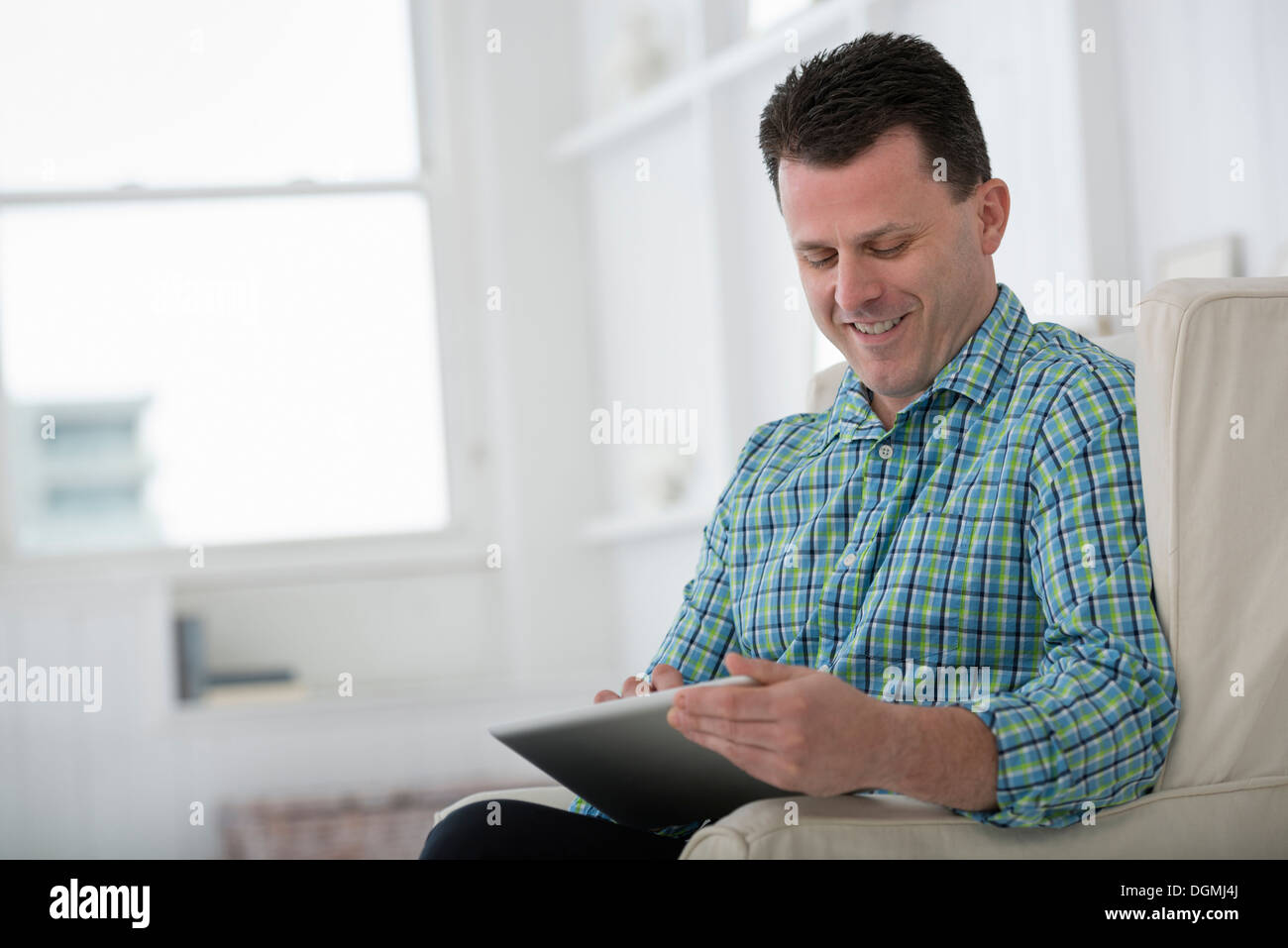 A man sitting in an armchair, using a digital tablet. Stock Photo