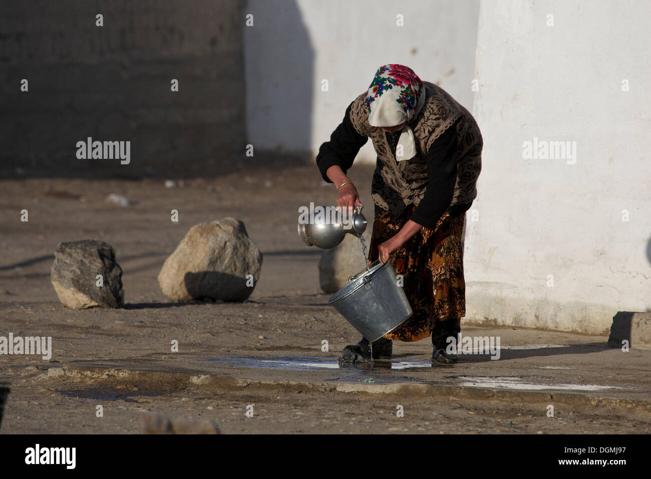 Kirghiz woman washing tin bucket with a water carafe in Alichur on the Pamir Highway M41, Pamir, Tajikistan, Central Asia, Asia Stock Photo