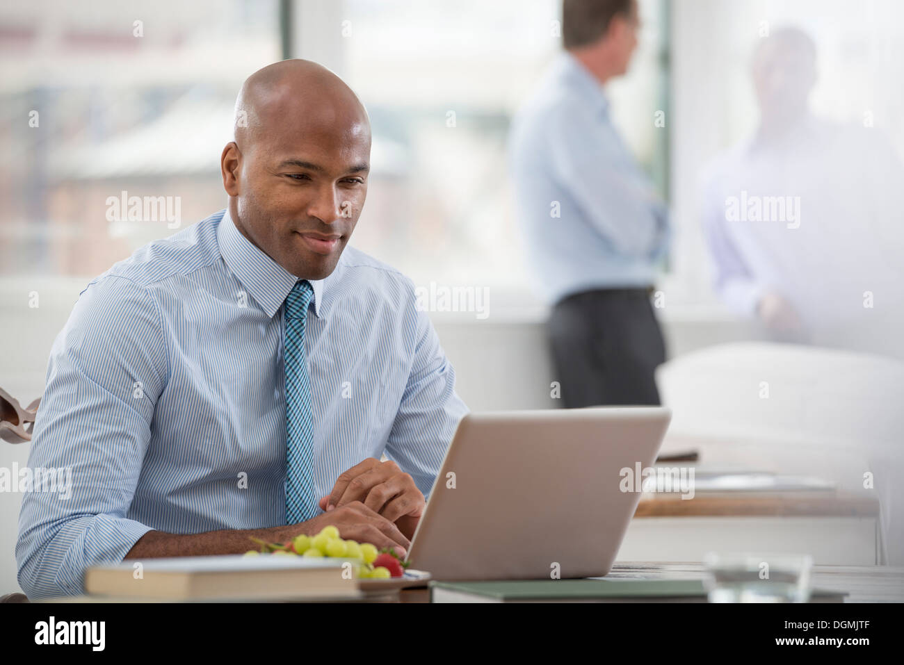 Office life. A businessman in a shirt and tie sitting at a desk, using a laptop computer. Stock Photo