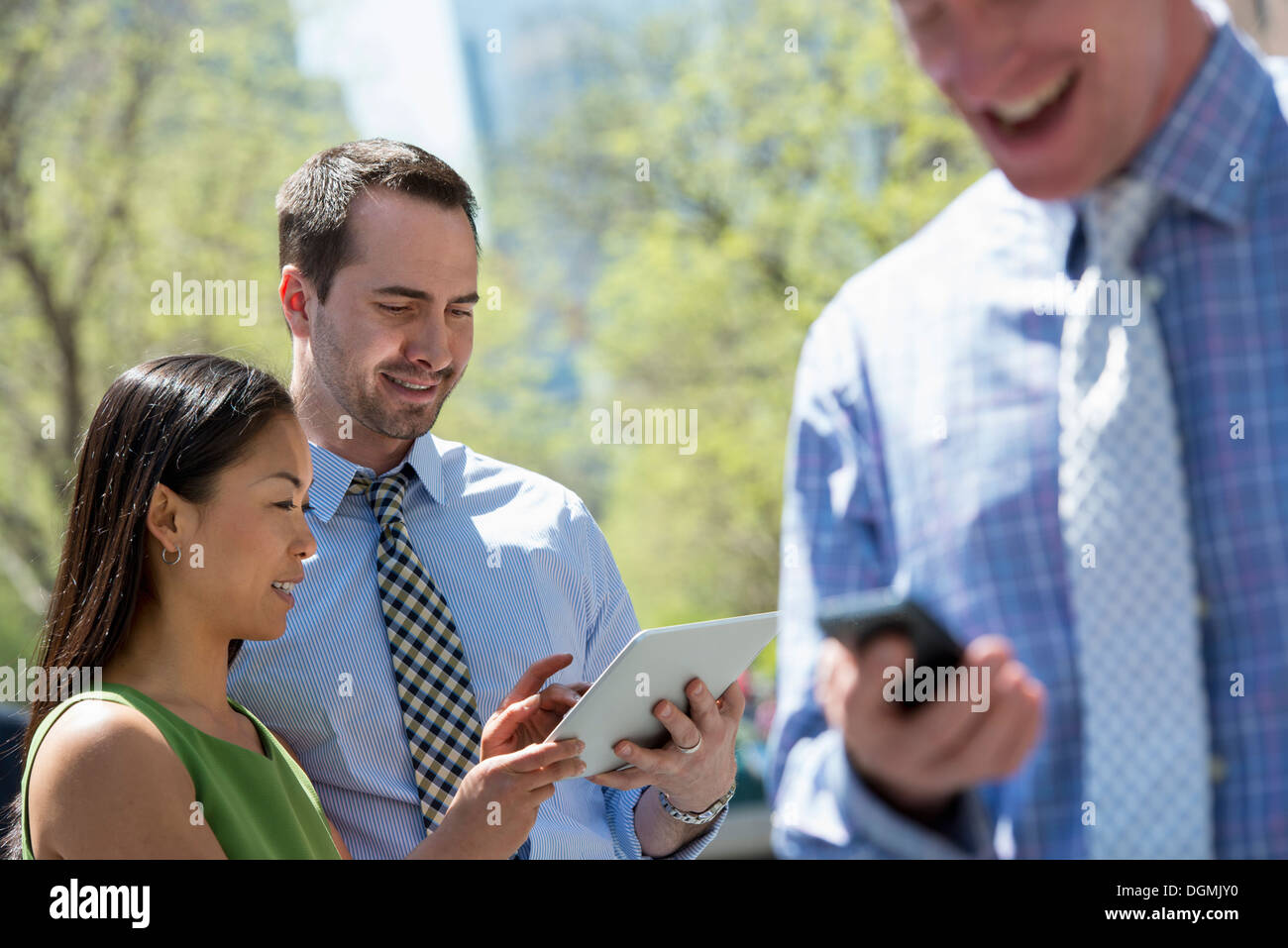 A businesswoman and two businessmen outdoors in the city. Checking their phones. Stock Photo