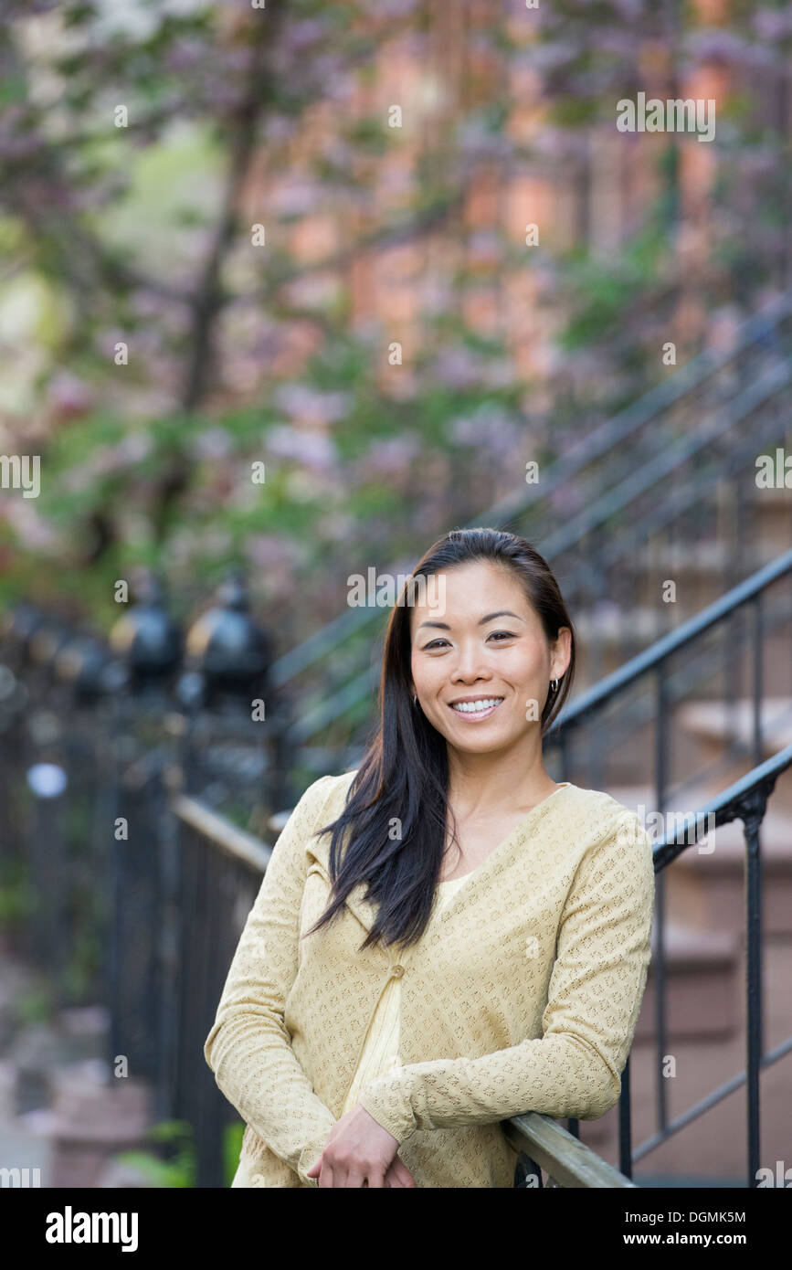 A young woman with long black hair, leaning on a railing at the bottom of a flight of steps. Stock Photo
