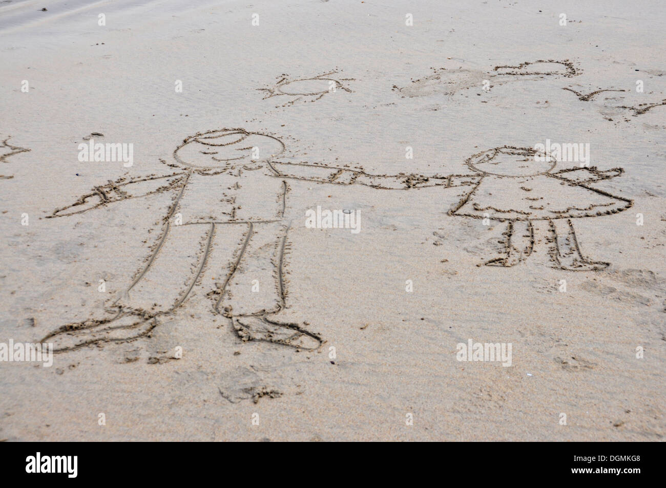 On a sandy beach - drawing with a stick in the sand - simple outlines - boy and girl  holding hands - the sun  - and birds Stock Photo