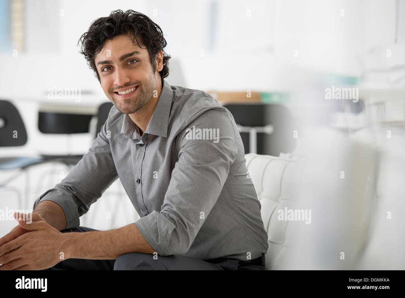 Business. A man seated with his hands clasped in a relaxed pose. Smiling and leaning forwards. Stock Photo