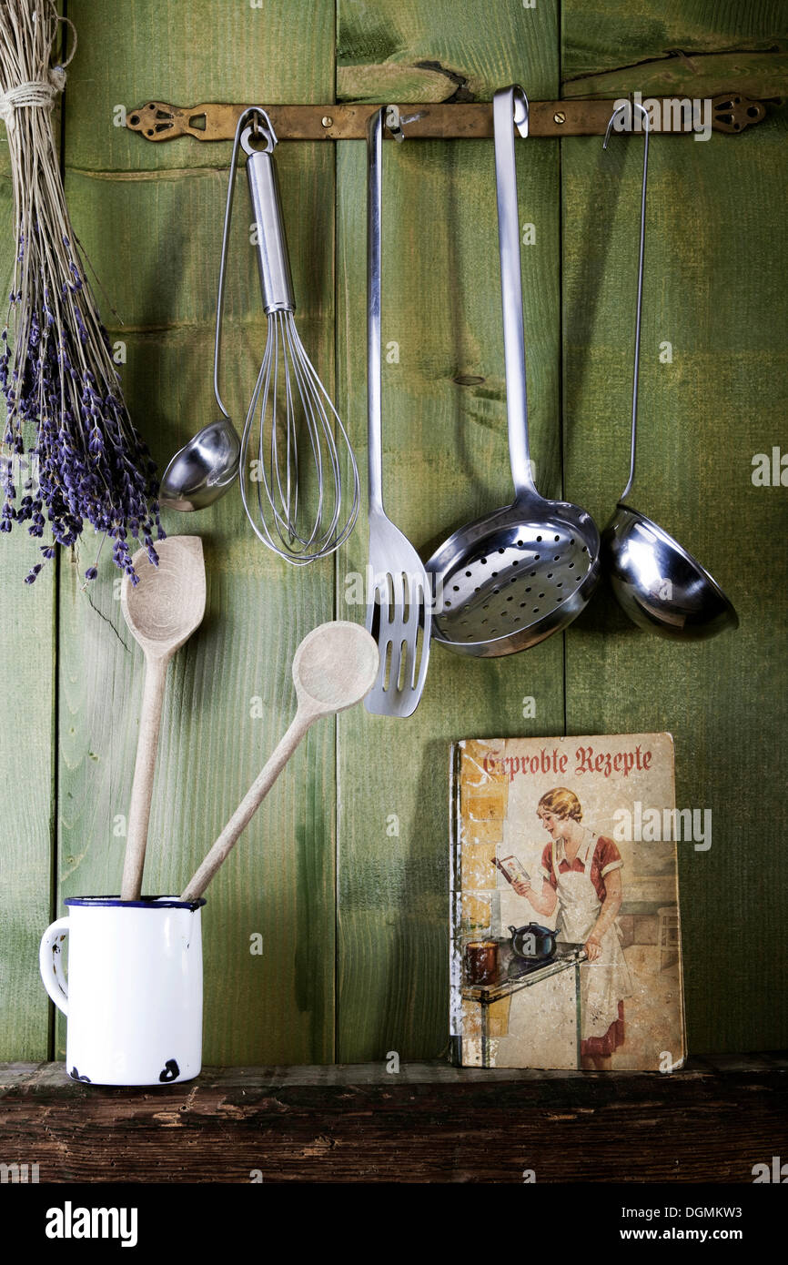 Old cookbook with cooking utensils in front of a green wooden wall, Germany Stock Photo