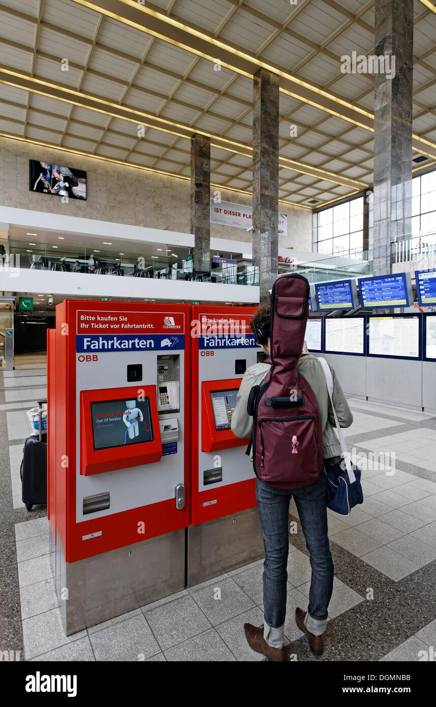 Young man with a guitar on his back buying a train ticket at ticket machine of the OeBB, Oesterreichische Bundesbahnen Stock Photo