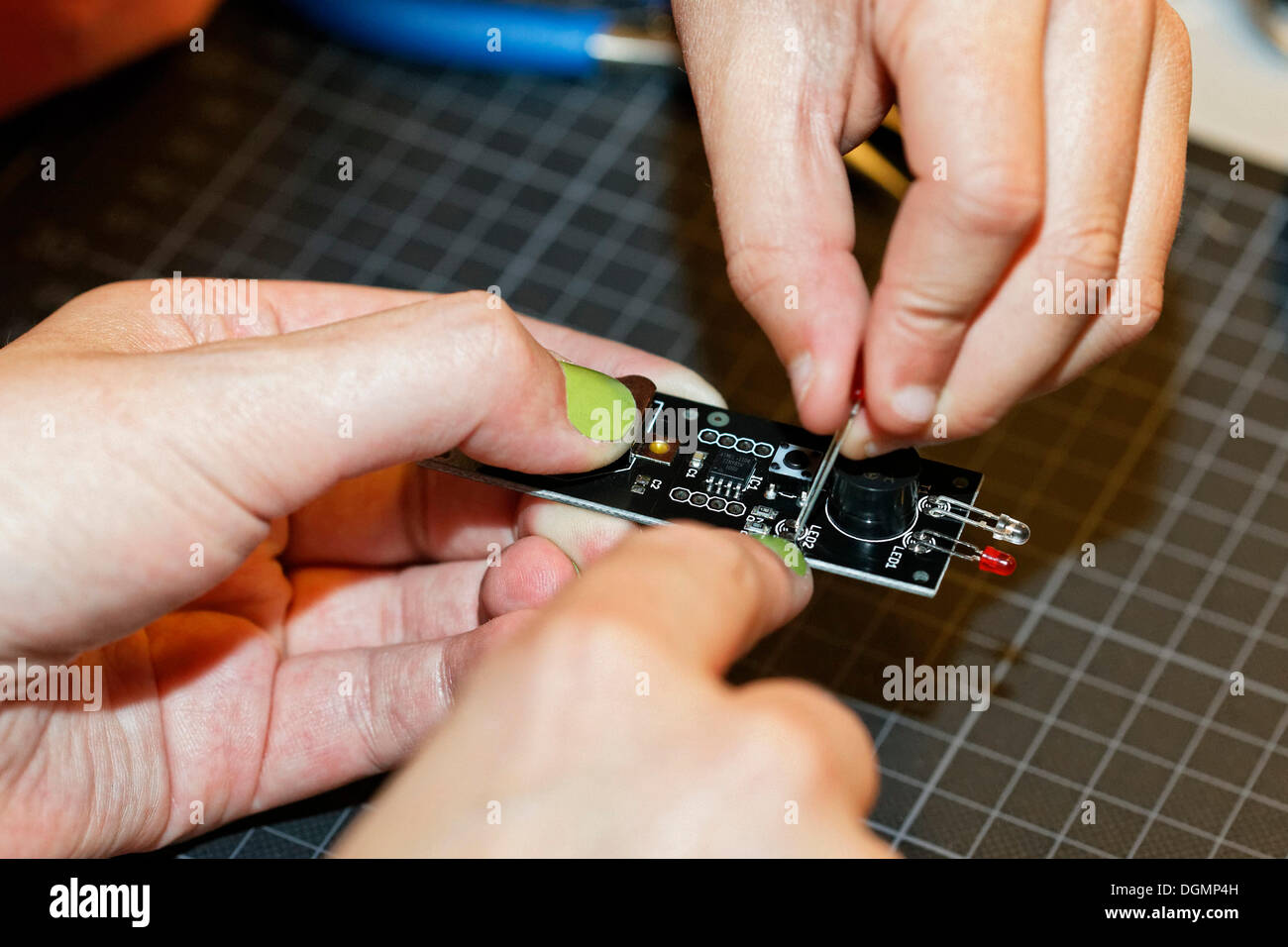 Hand with painted nails and a child's hand working together on an electronic device with light emitting diodes, IdeenPark 2012, Stock Photo