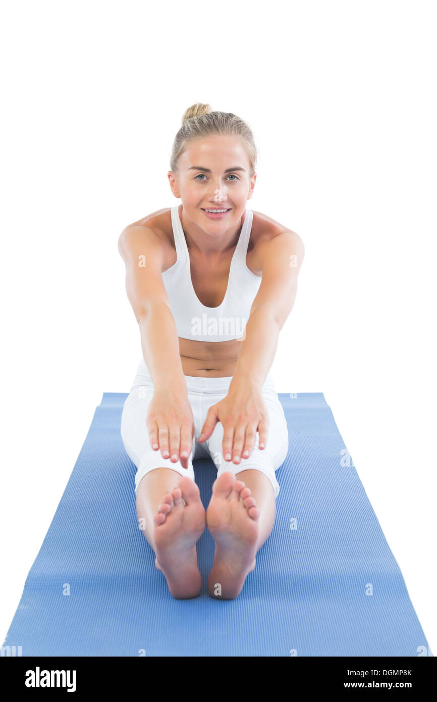 Toned smiling blonde sitting on exercise mat stretching legs Stock Photo