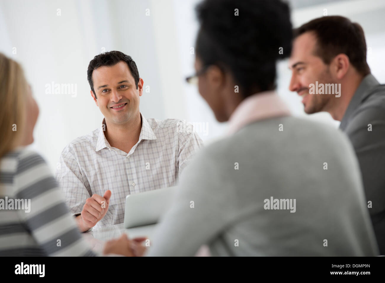 Office interior. A group of four people, two men and two women, seated around a table. Business meeting. Stock Photo