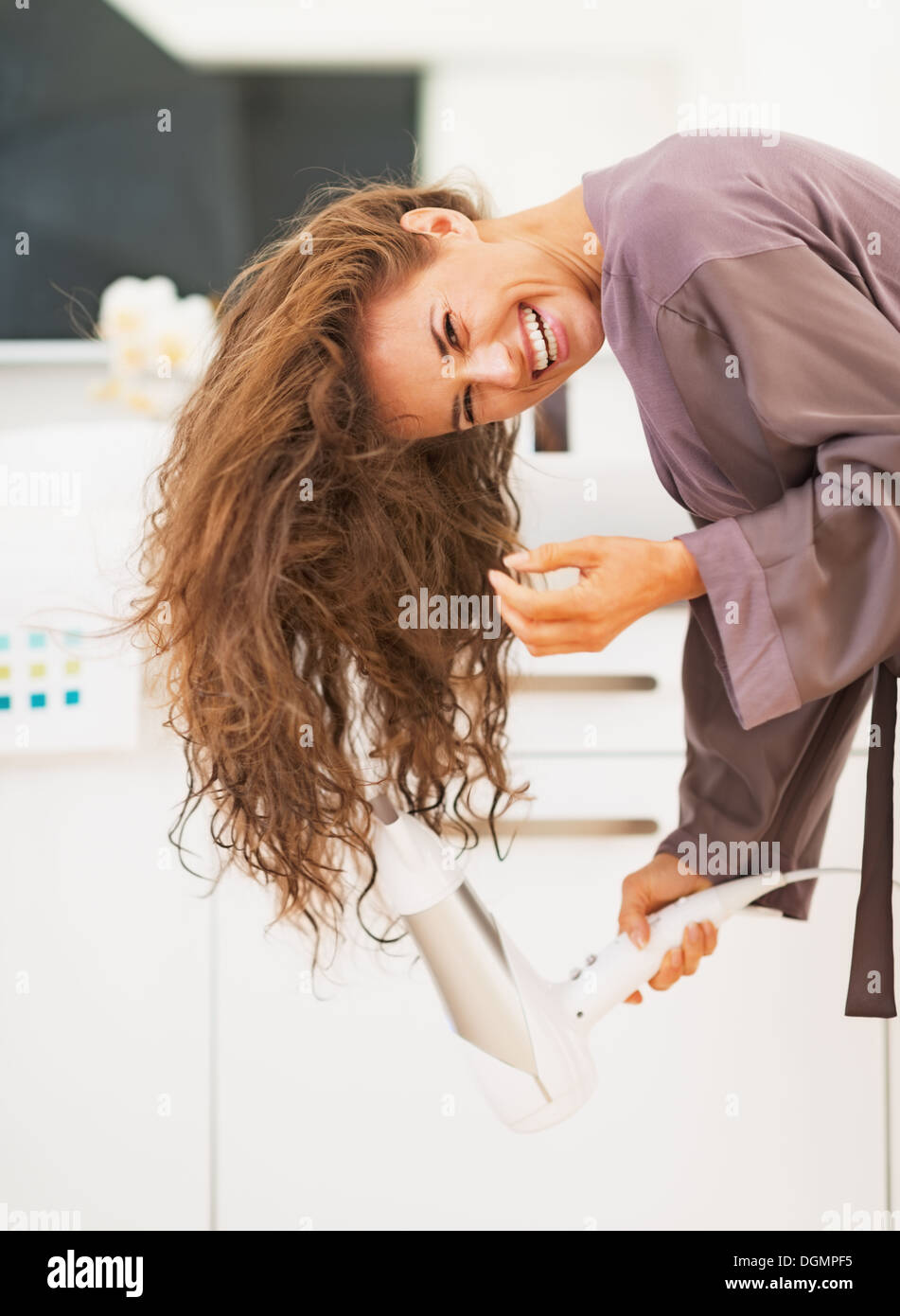 Smiling young woman blow drying hair in bathroom Stock Photo - Alamy