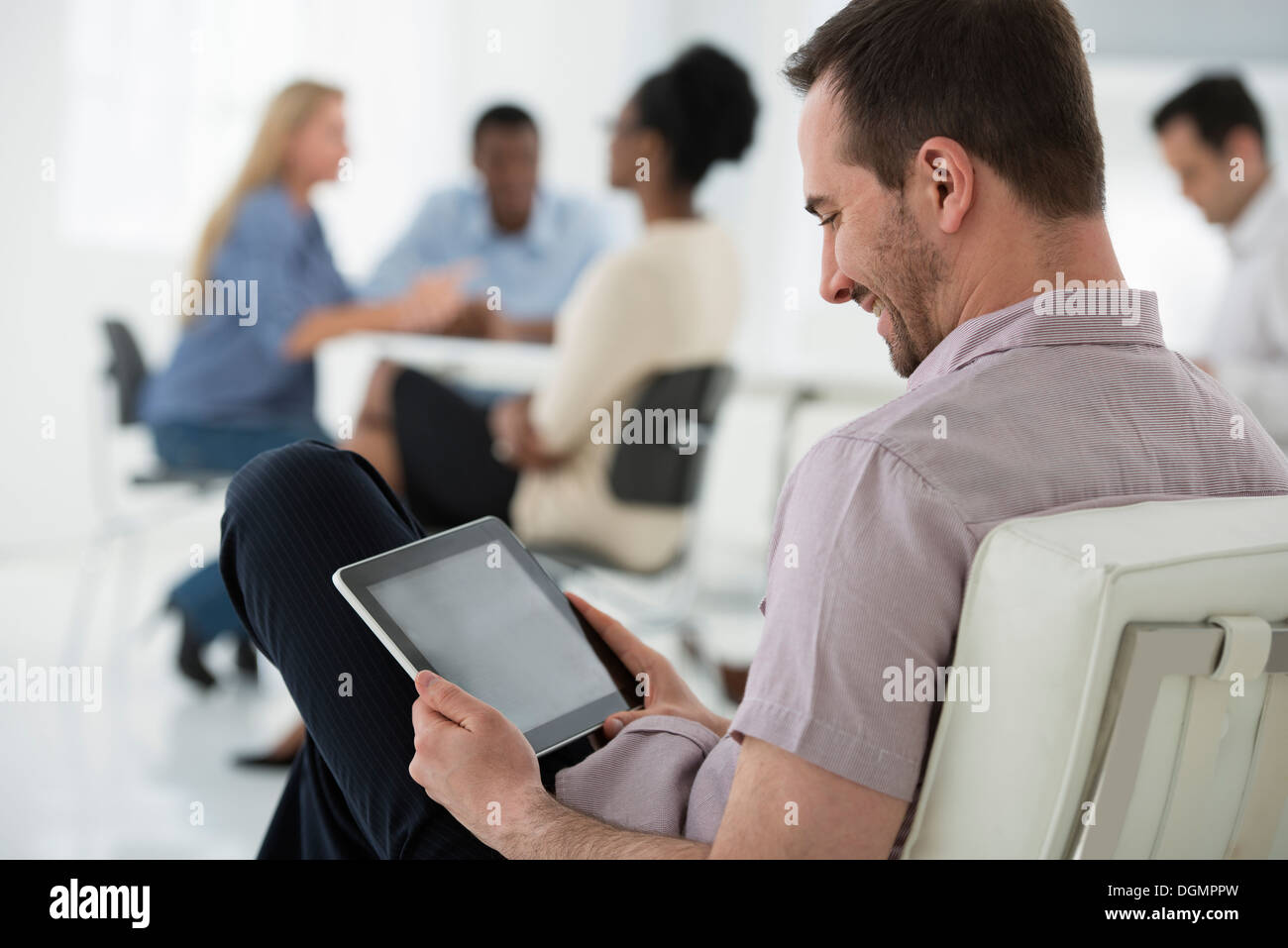Office interior. Meeting. One person seated separately, using a tablet computer. Stock Photo