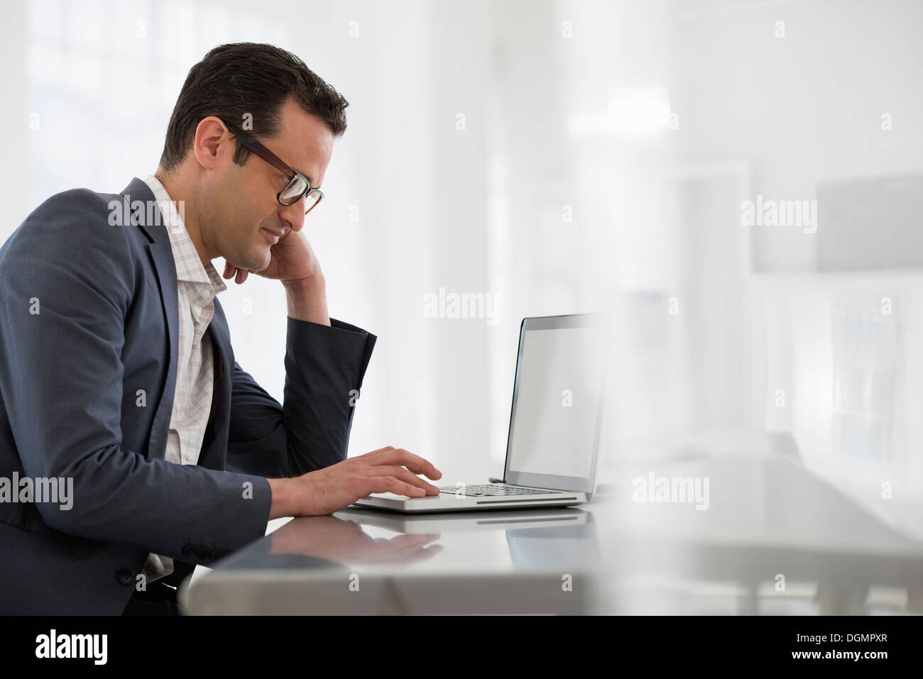 Office interior. A businessman seated at a table, using a laptop computer. Stock Photo